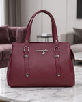A burgundy leather handbag with silver-tone hardware, displayed on a white marble table in a modern living room setting.