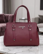 A burgundy leather handbag with silver-tone hardware, displayed on a white marble table in a modern living room setting.