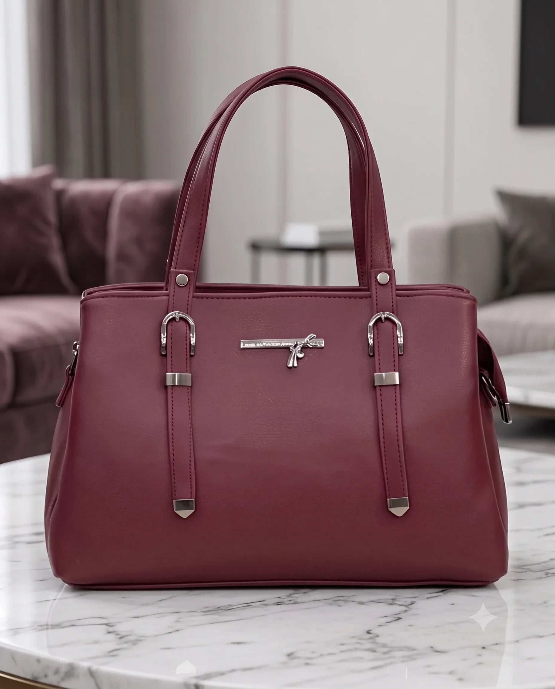 A burgundy leather handbag with silver-tone hardware, displayed on a white marble table in a modern living room setting.