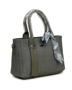 Gray handbag with a green strap and a gray scarf tied around the handle on a white background