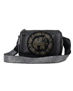 Black crossbody bag with decorative emblem and striped strap on a white background